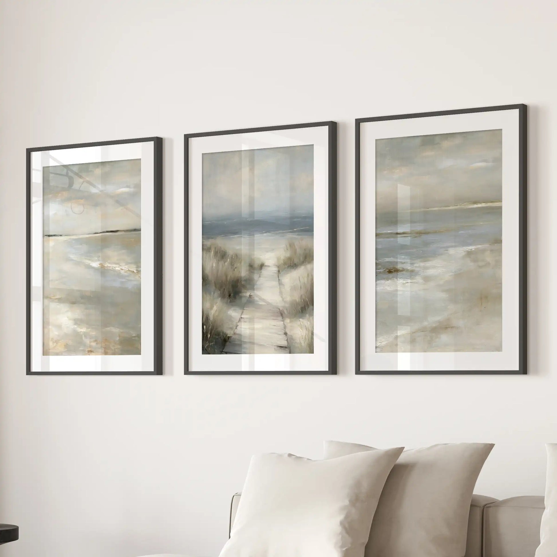 Dune grass shoreline trio of prints in black frames with wide mats brings airy coastal wall art to the living room, styled behind the couch.