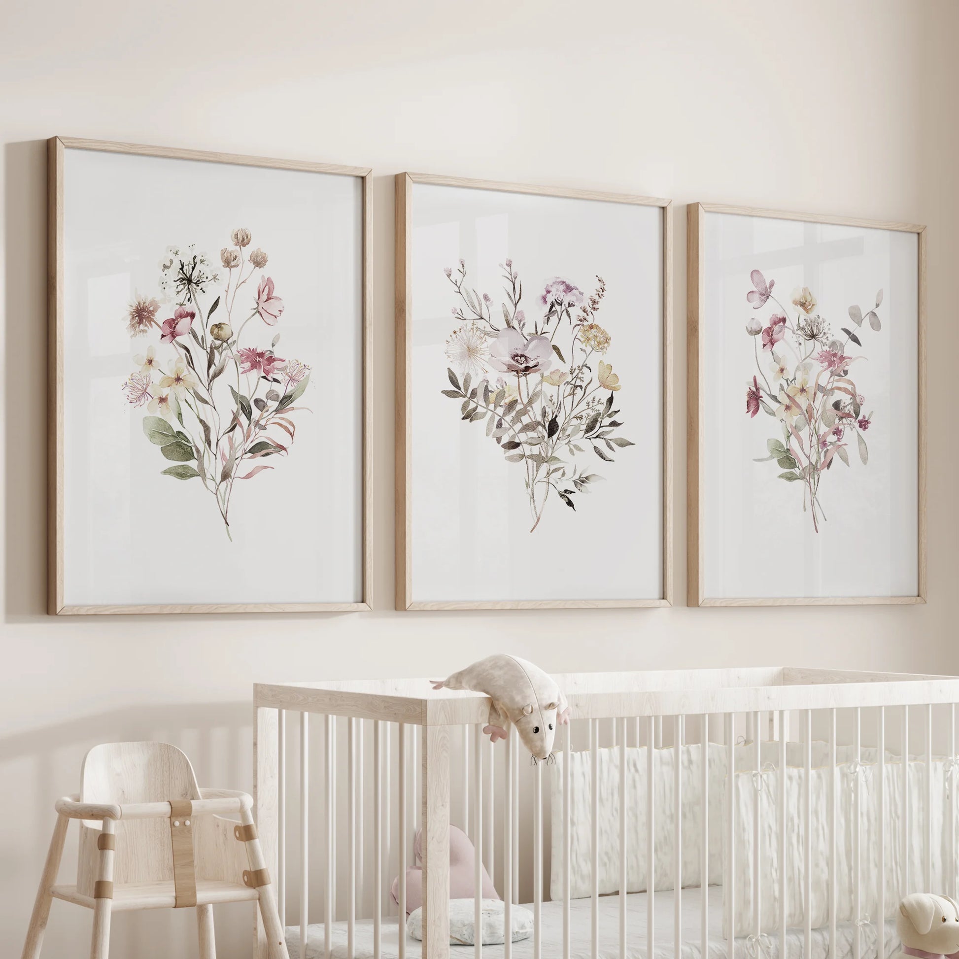 A trio of watercolored wildflowers in slender wood frames hangs above the bassinet, lending the nursery a tender botanical calm.