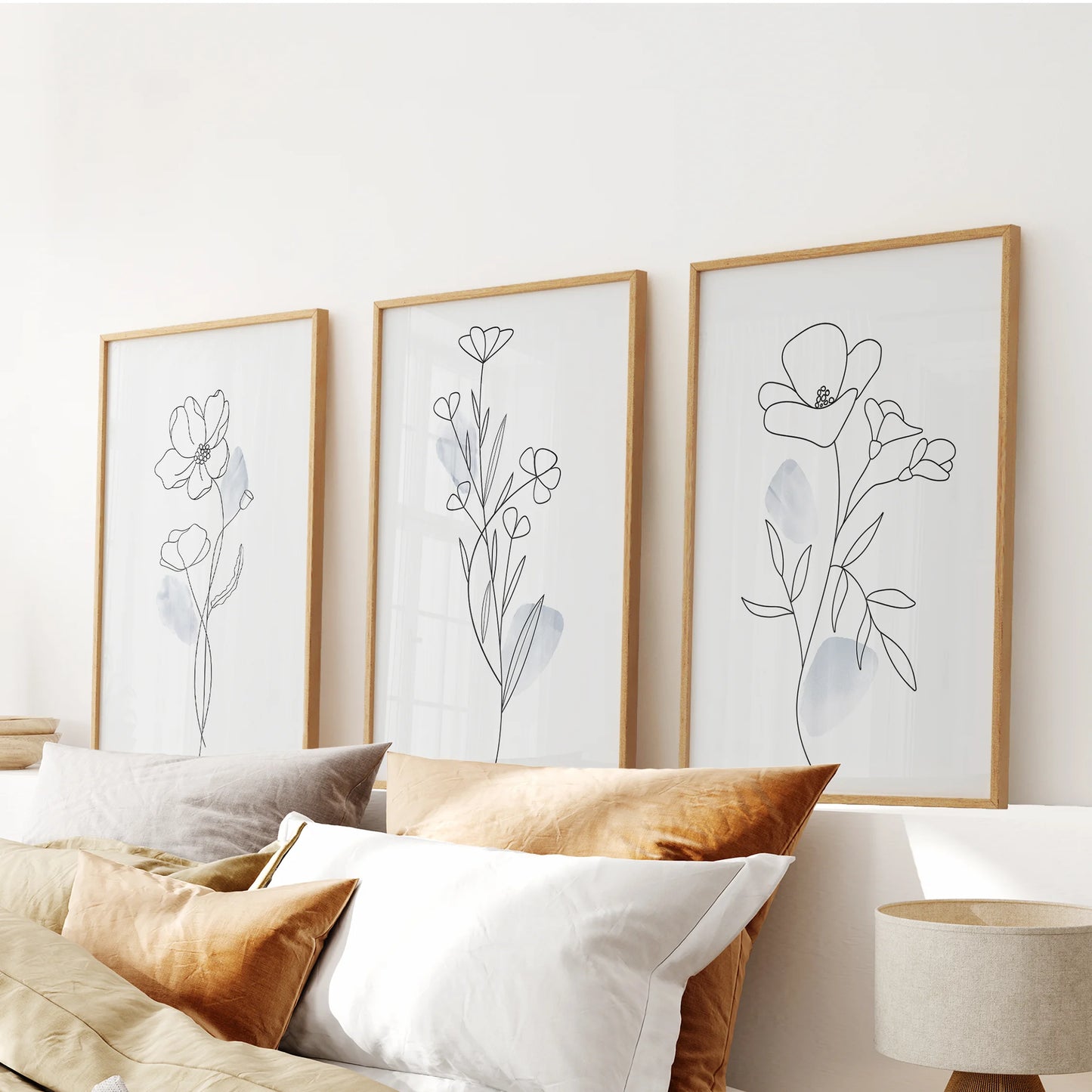 A warm wood-framed trio of gentle blue floral prints floats over the bed’s headboard, completing a soft, modern wall display.