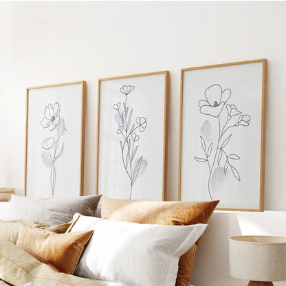 A warm wood-framed trio of gentle blue floral prints floats over the bed’s headboard, completing a soft, modern wall display.