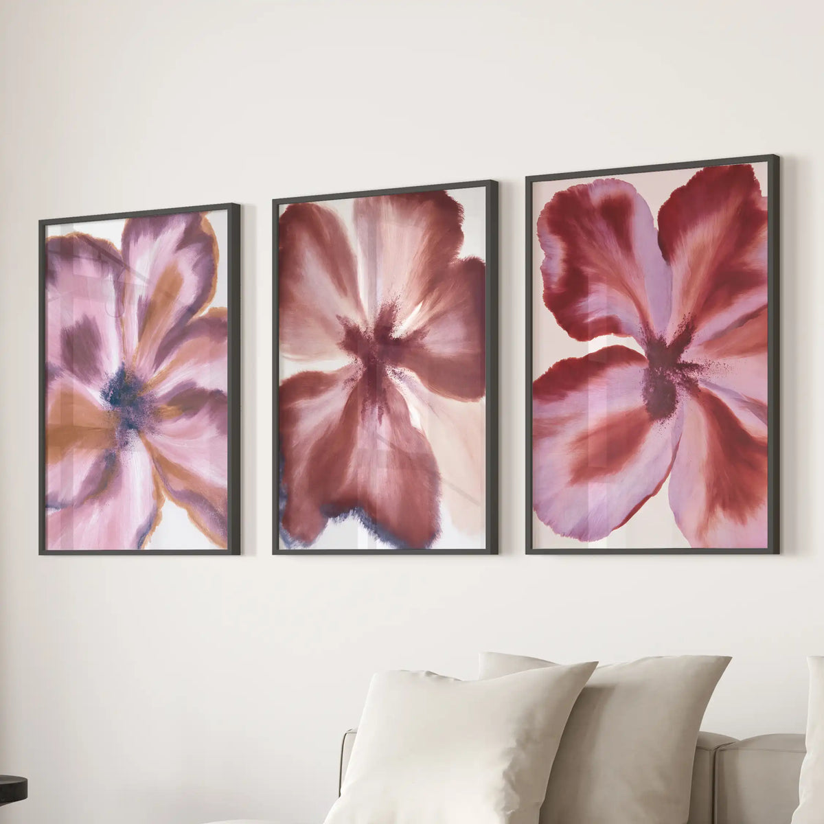 Black frames hold three abstract burgundy flower prints above a sofa.