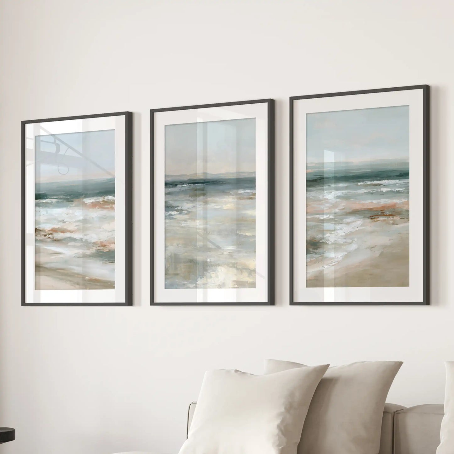 Three shoreline prints in black-matted frames form sleek wall art over the sectional sofa, giving the sitting room a quiet coastal rhythm.