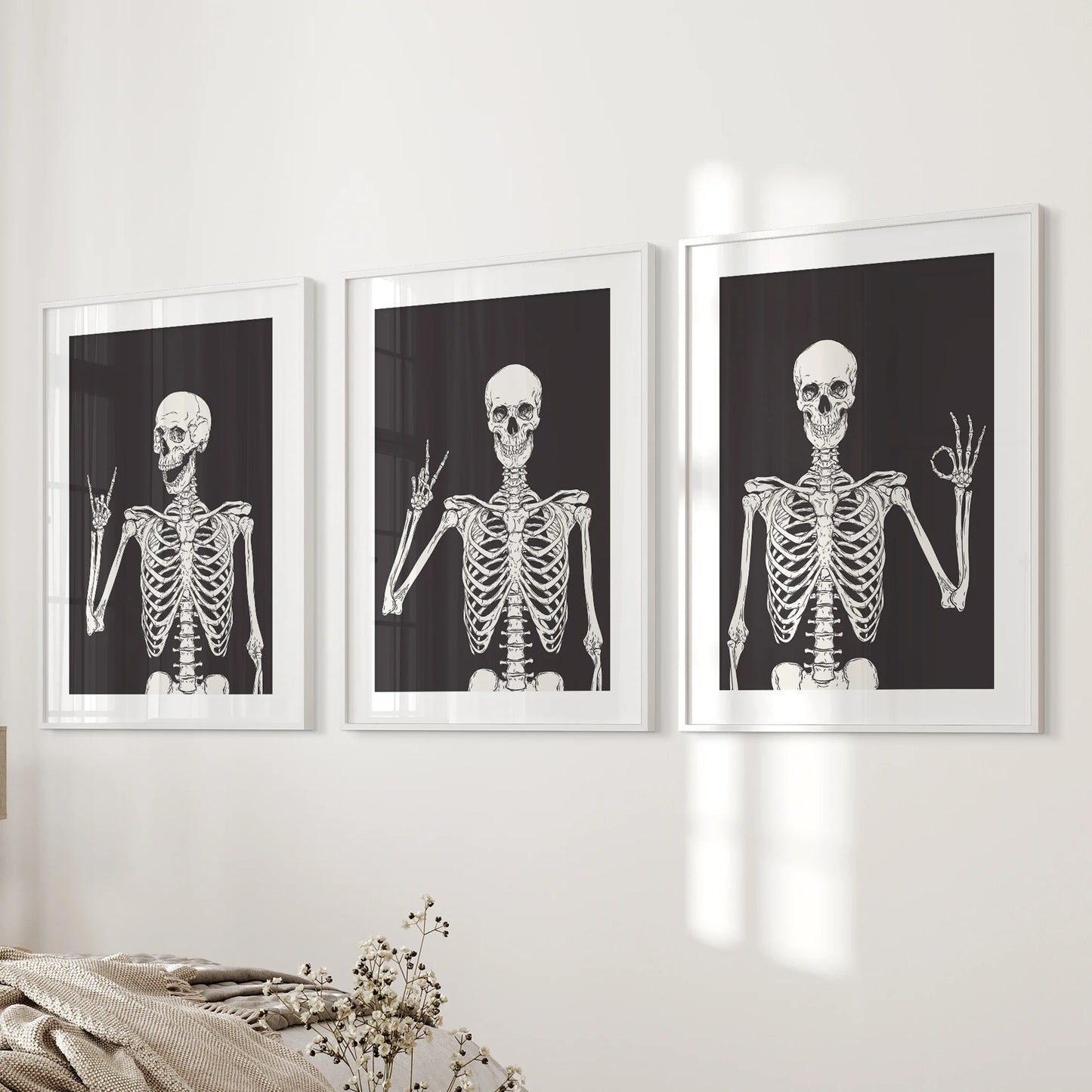 A modern set of three skeleton artworks, framed with white mats, rests on the bedroom wall beside the bed for a subtle Halloween touch.