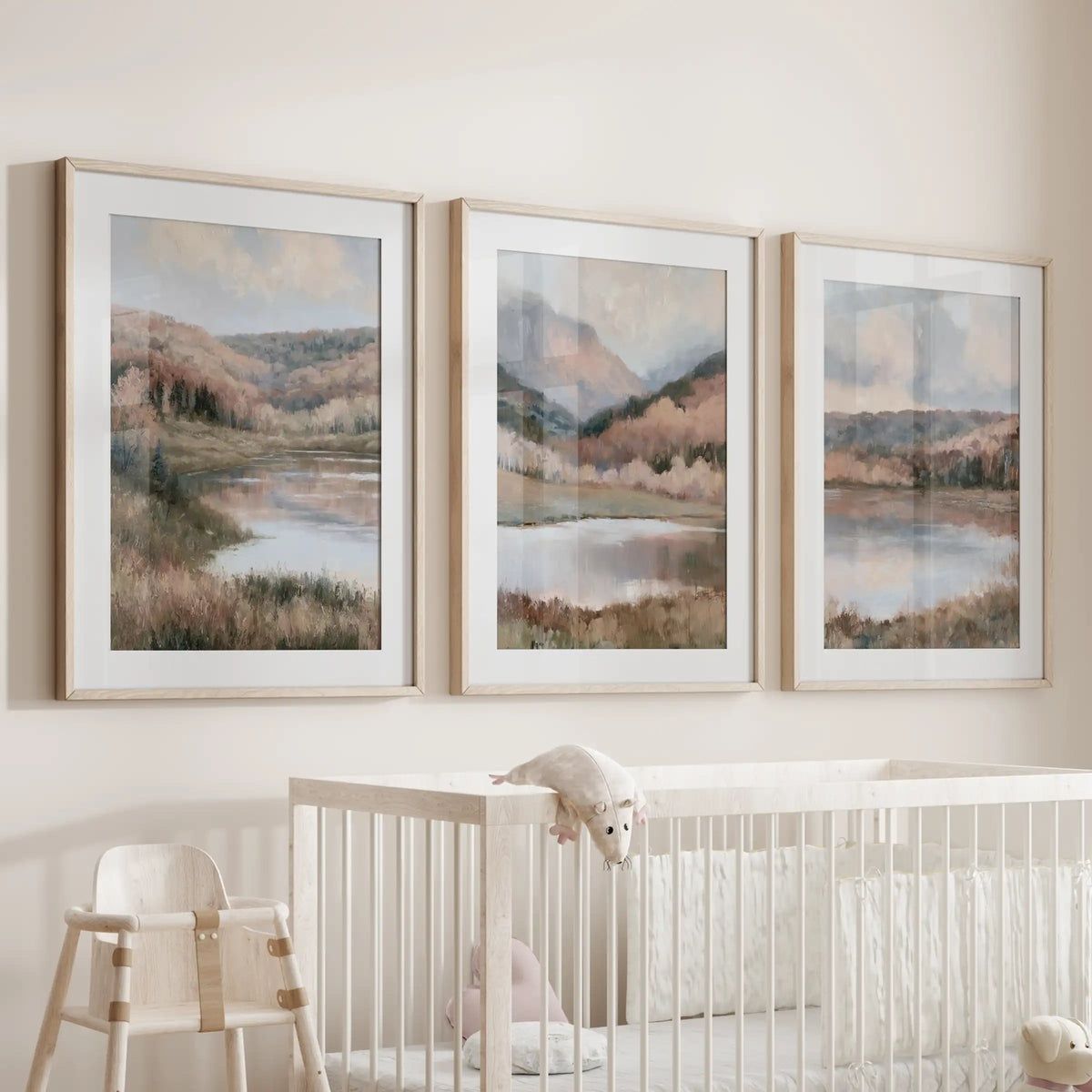 A three-piece art set of impressionist lake landscapes, matted in natural wood frames, hangs over the nursery bassinet with muted shoreline hues.