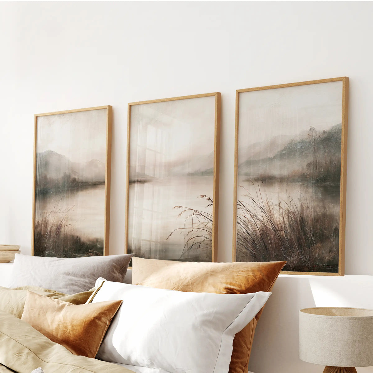 Set of three painterly nature wall hangings in light oak frames, arranged above the bed in a bedroom.
