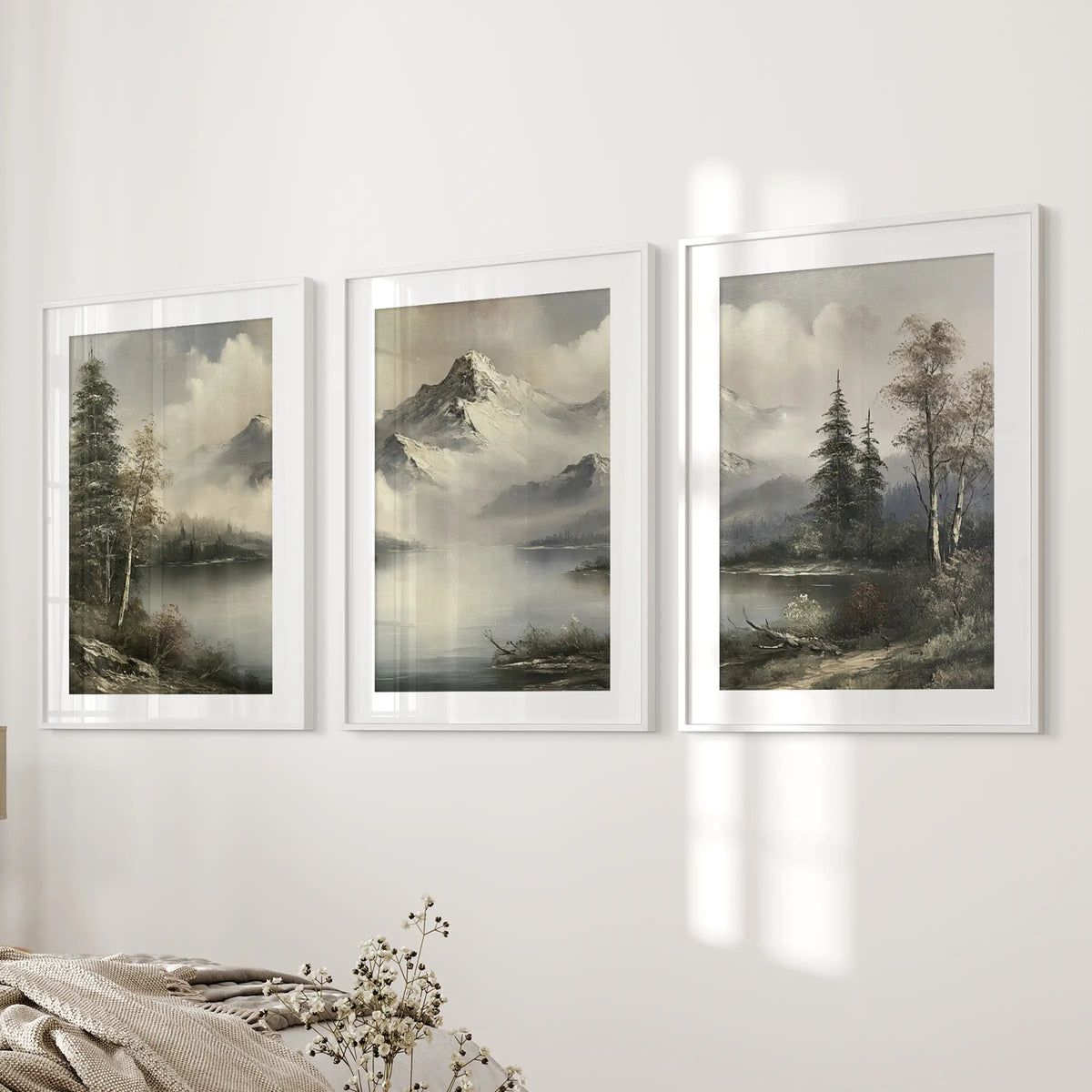 Set of three mountain cabin landscape art prints in white frames with mats, arranged on the bedroom wall beside the bed.