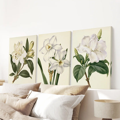 White botanical flowers are displayed on three canvases above a bed.