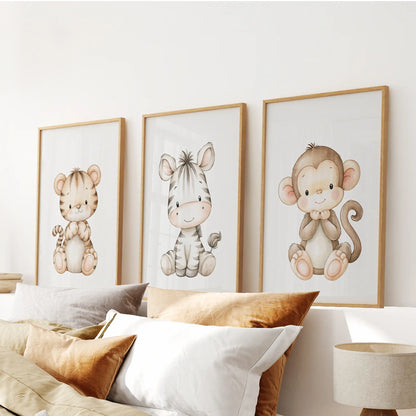 A small brown monkey with a curled tail sits beside a striped zebra and tiger cub in three oak-framed prints above a bed.