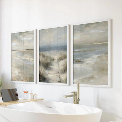 A three-panel white-framed wall art of a beach path through dunes hangs above the bath, giving the bathroom a spa-light coastal accent.