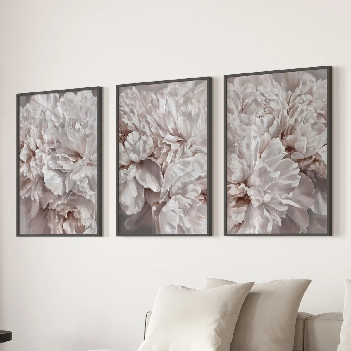 Above a sofa, three prints in black frames show densely layered peony petals filling each picture.