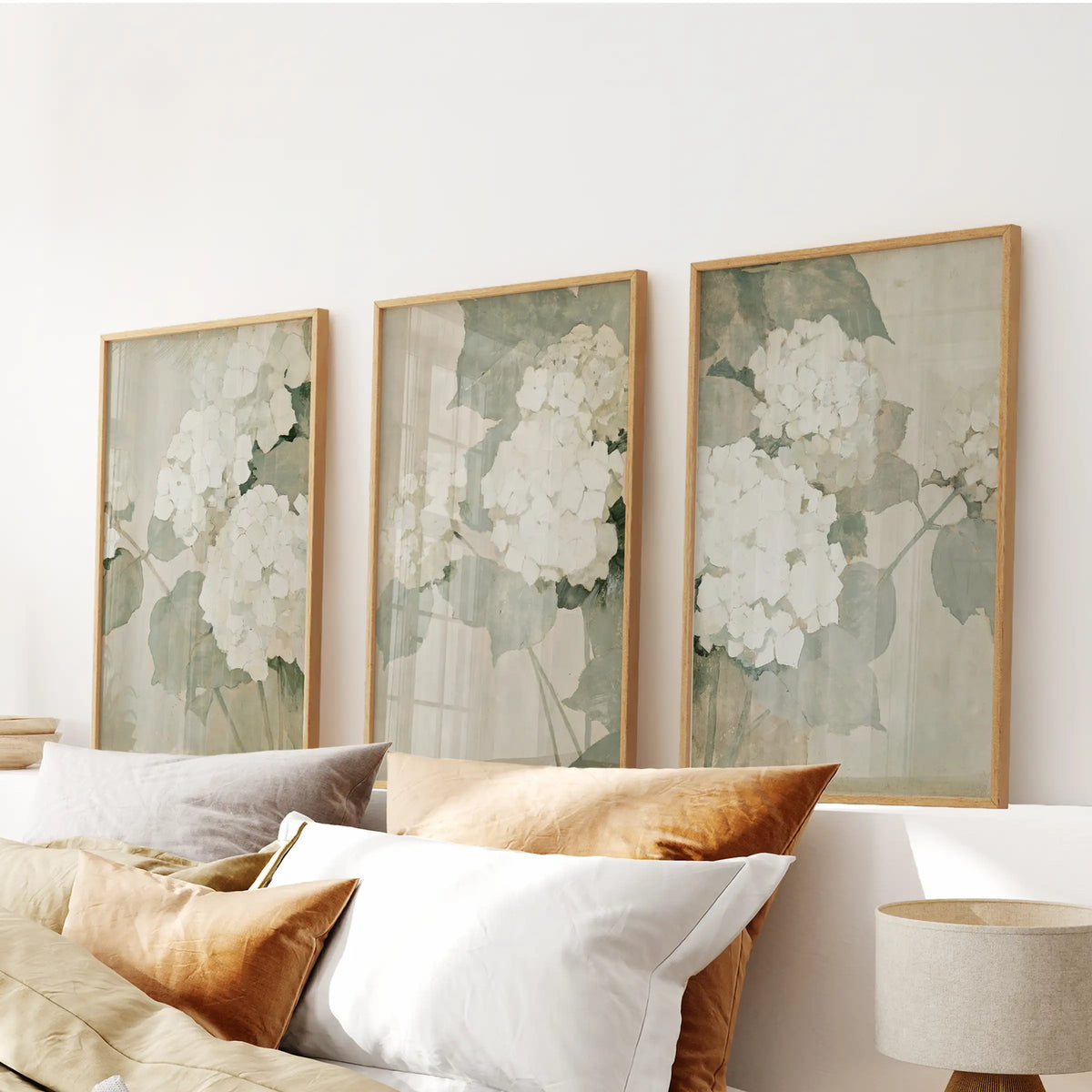 Three-piece wall art set of soft white flowers in oak frames, hanging above the headboard in a bedroom.
