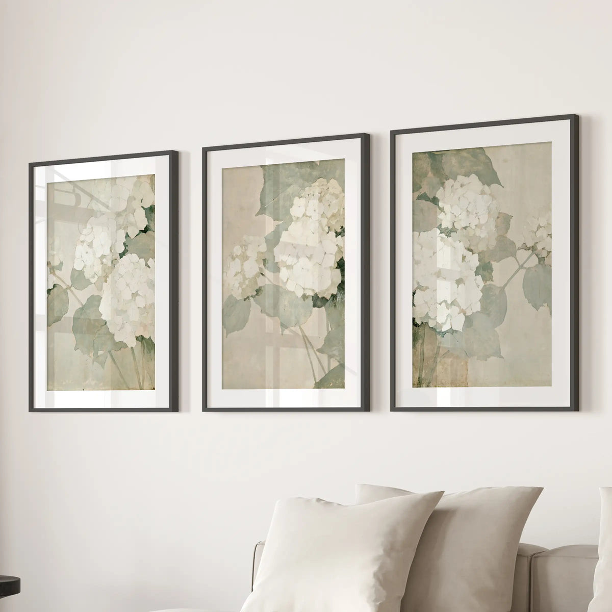 Neutral hydrangea blooms form a wall art trio in black matted frames, displayed over a sectional sofa in the lounge.