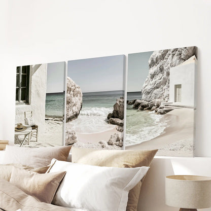 A 3-print gallery on gallery-wrapped canvas features calm shoreline photography, positioned above the headboard to ground the bedroom in soft Mediterranean neutrals.
