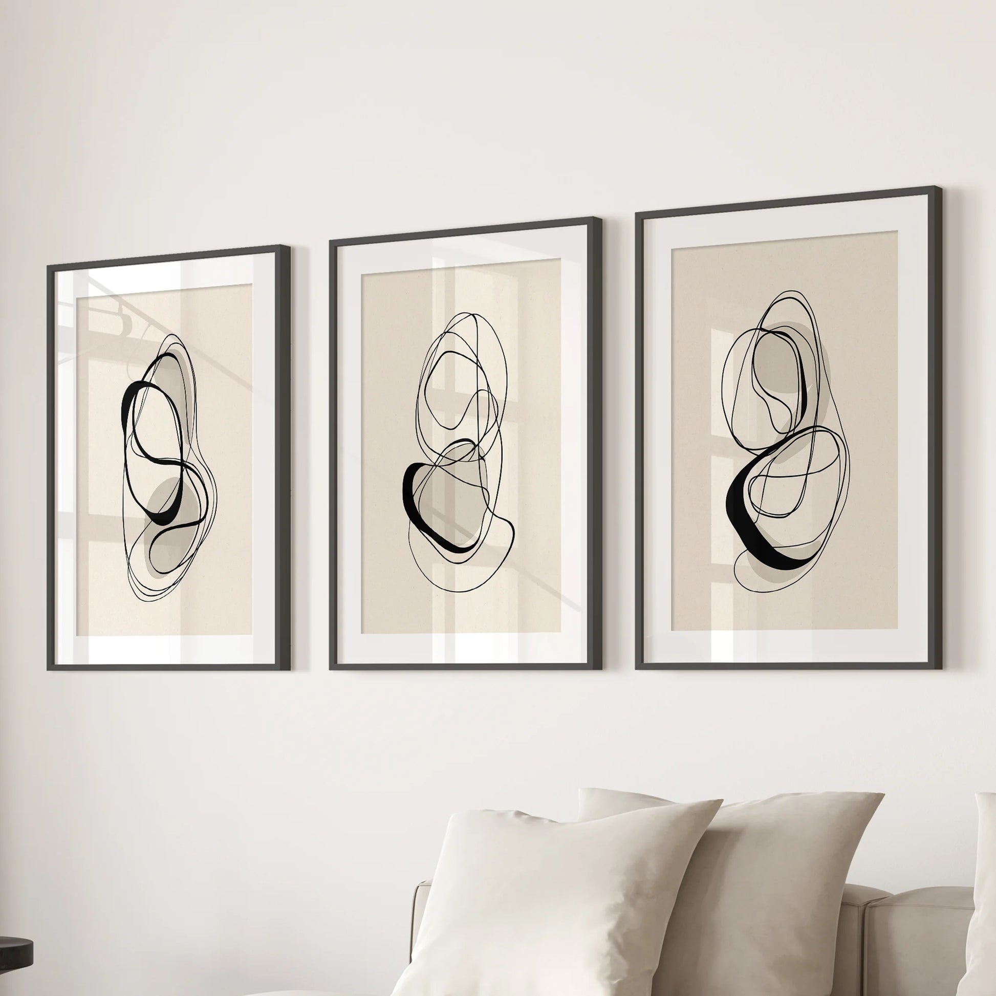 Trio of abstract black-and-beige prints in wide-matted black frames, giving the living-room wall behind the couch a polished, modern balance.