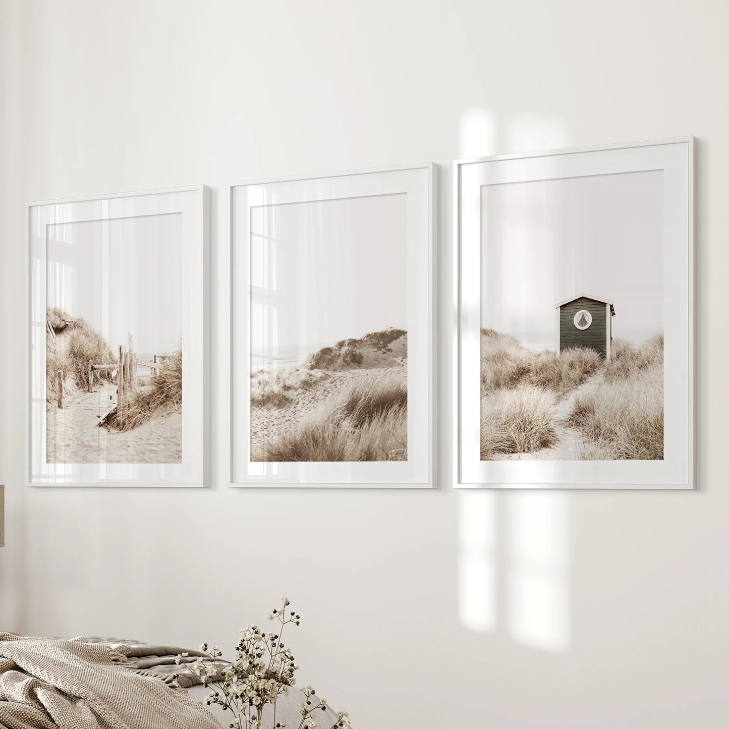 Pampas grass three-print poster set in white mat frames sits beside the bed in the bedroom, bringing airy plumes and subtle coastal warmth.