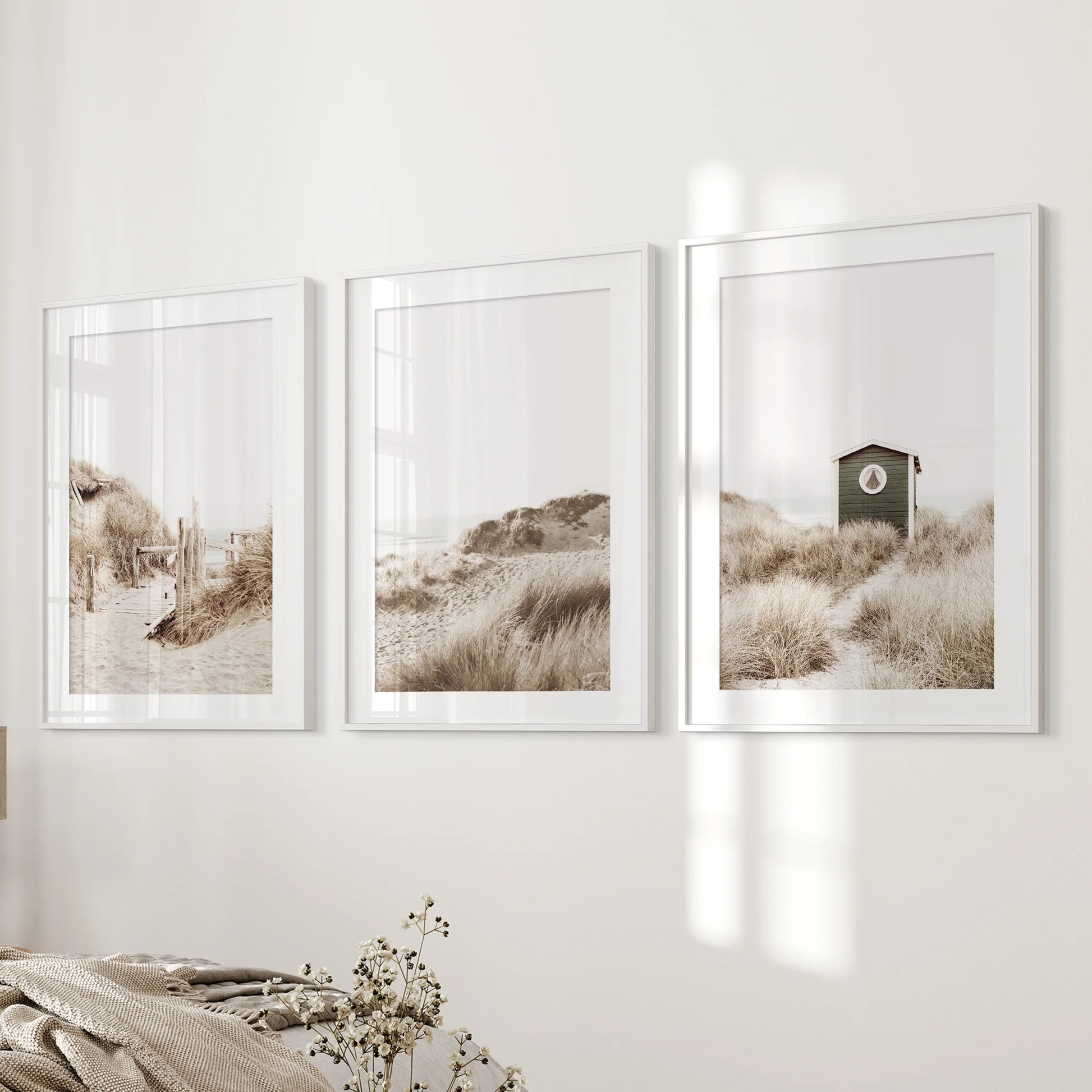 Pampas grass three-print poster set in white mat frames sits beside the bed in the bedroom, bringing airy plumes and subtle coastal warmth.