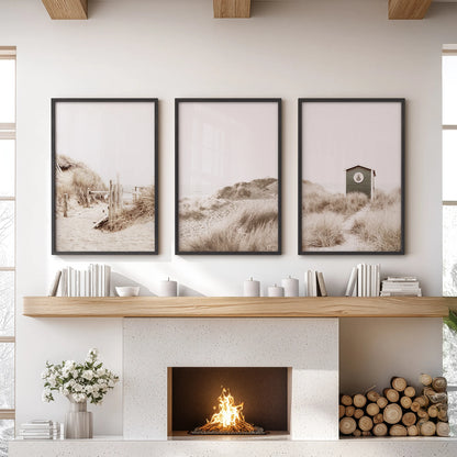 A trio of black-framed wall prints shows a sunlit beach path above the lounge mantel, bringing airy dunes and a calm coastal mood.