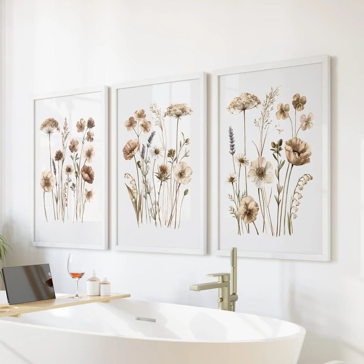 A set of three neutral wildflower prints in white frames above a freestanding bathtub.