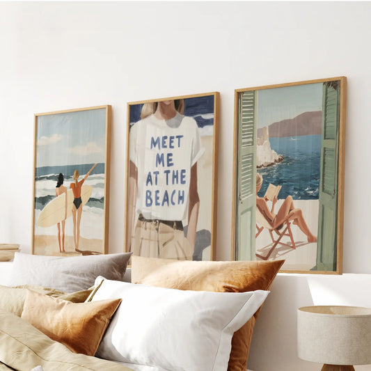 Coastal 3 piece wall art with surfers, Meet Me at the Beach typography and ocean view prints in light oak frames above a bed to anchor a calm, airy bedroom centerpiece.