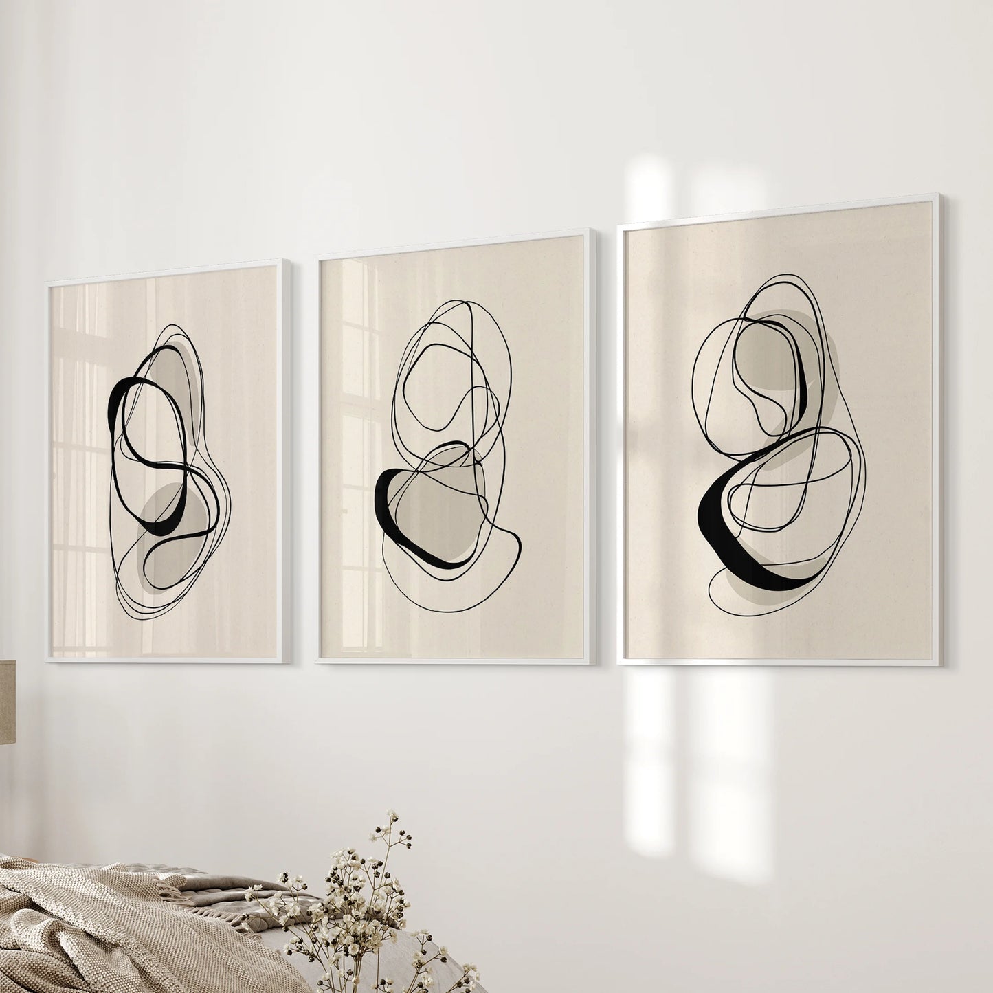A trio of abstract beige-and-black posters in white frames, arranged on the bedroom wall for a quiet, contemporary harmony.