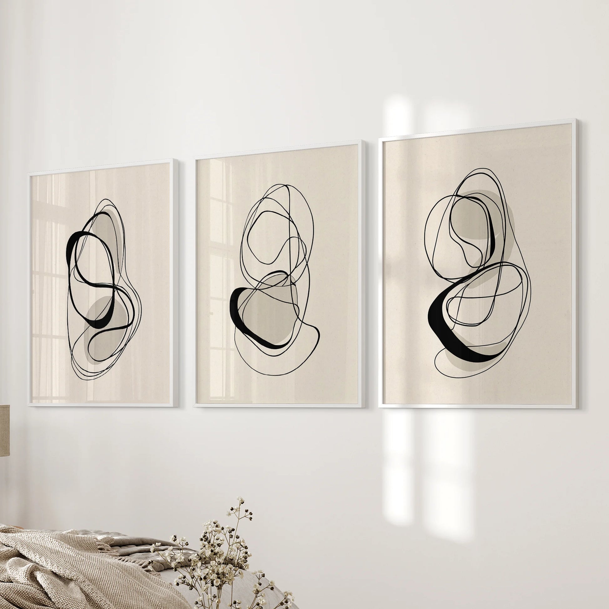 A trio of abstract beige-and-black posters in white frames, arranged on the bedroom wall for a quiet, contemporary harmony.