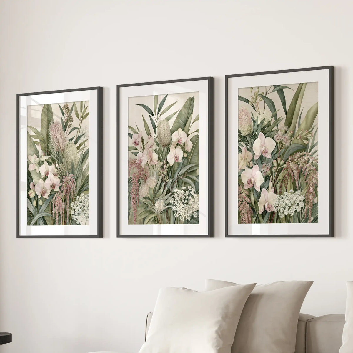 The three black frames above a sofa have white mats around dense foliage, pale orchids, rounded flower heads and small white blooms.