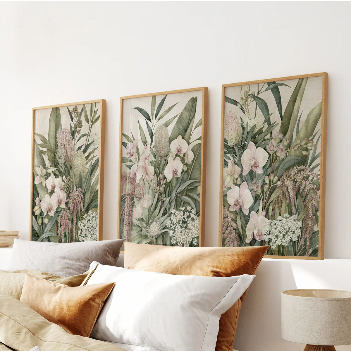 Orchids, rounded flower heads and fine sprays of white blooms fill three oak-framed prints above a bed, with layers of broad and narrow leaves.