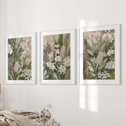 White mats border dense green leaves, pale orchids and rounded flower heads in three white-framed prints beside a bed.