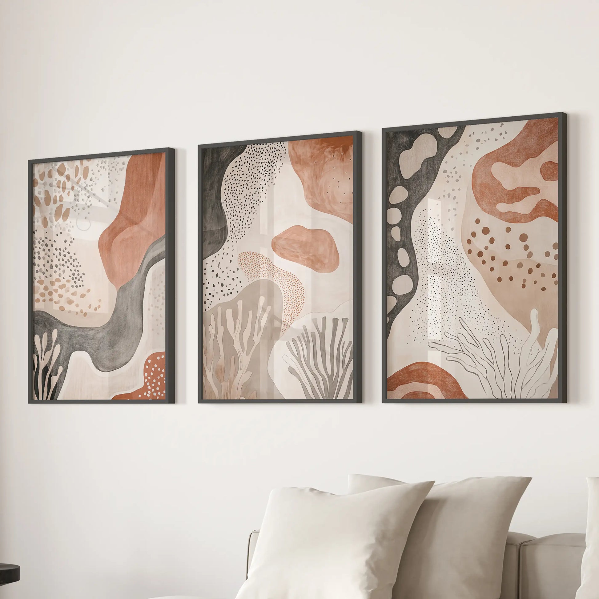 Set of three minimalist prints in slim black frames lines the wall behind the family-room couch, shaping a calm, grounded focal point.