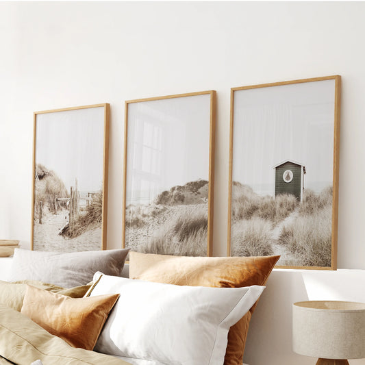 Over the bed, a three-piece oak-framed print set of sunlit dunes lines the wall with warm tones for an inviting coastal finish.