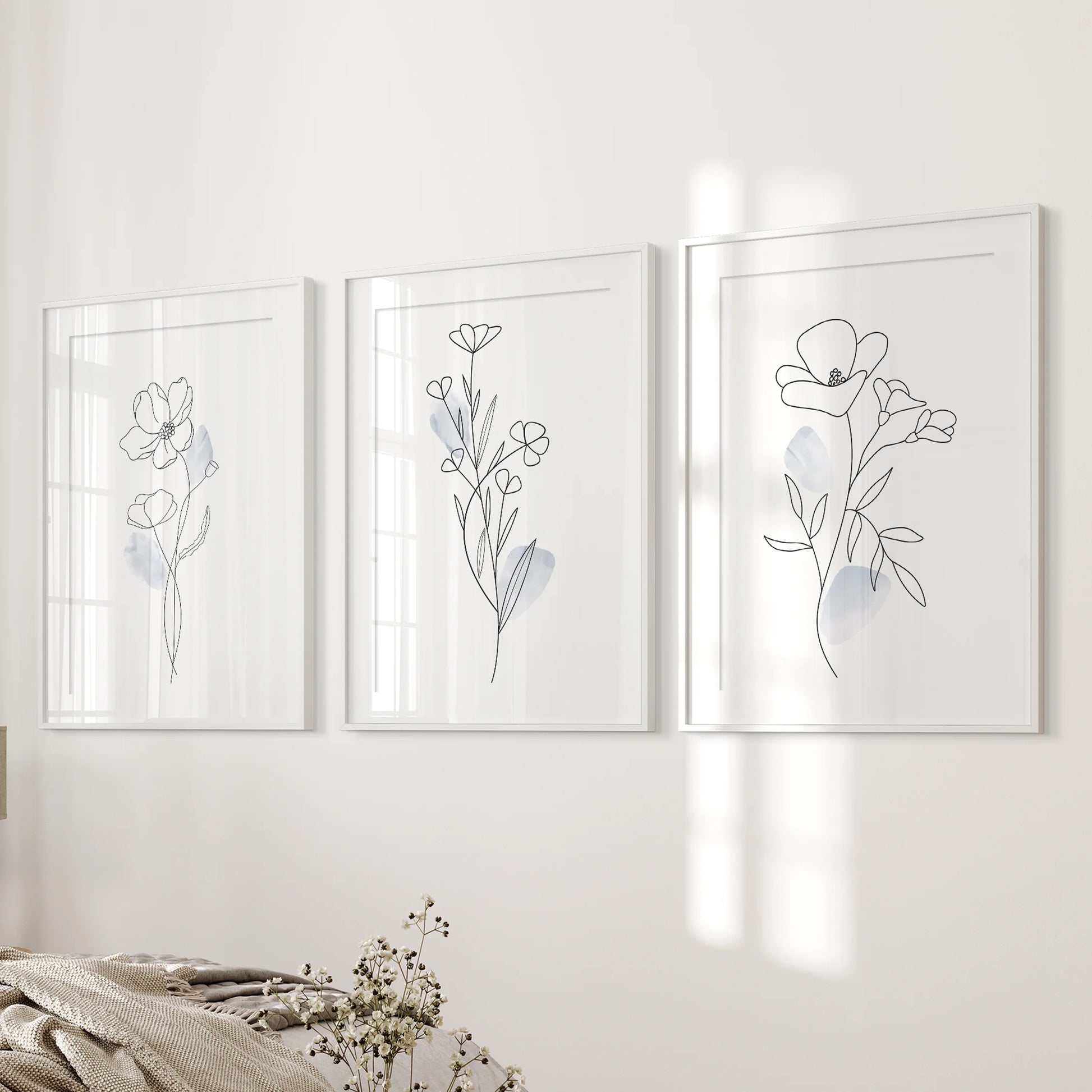 Abstract floral line sketches, 3 piece wall art in white frames with matting, rests near the bedroom’s bed wall for a serene, modern look.
