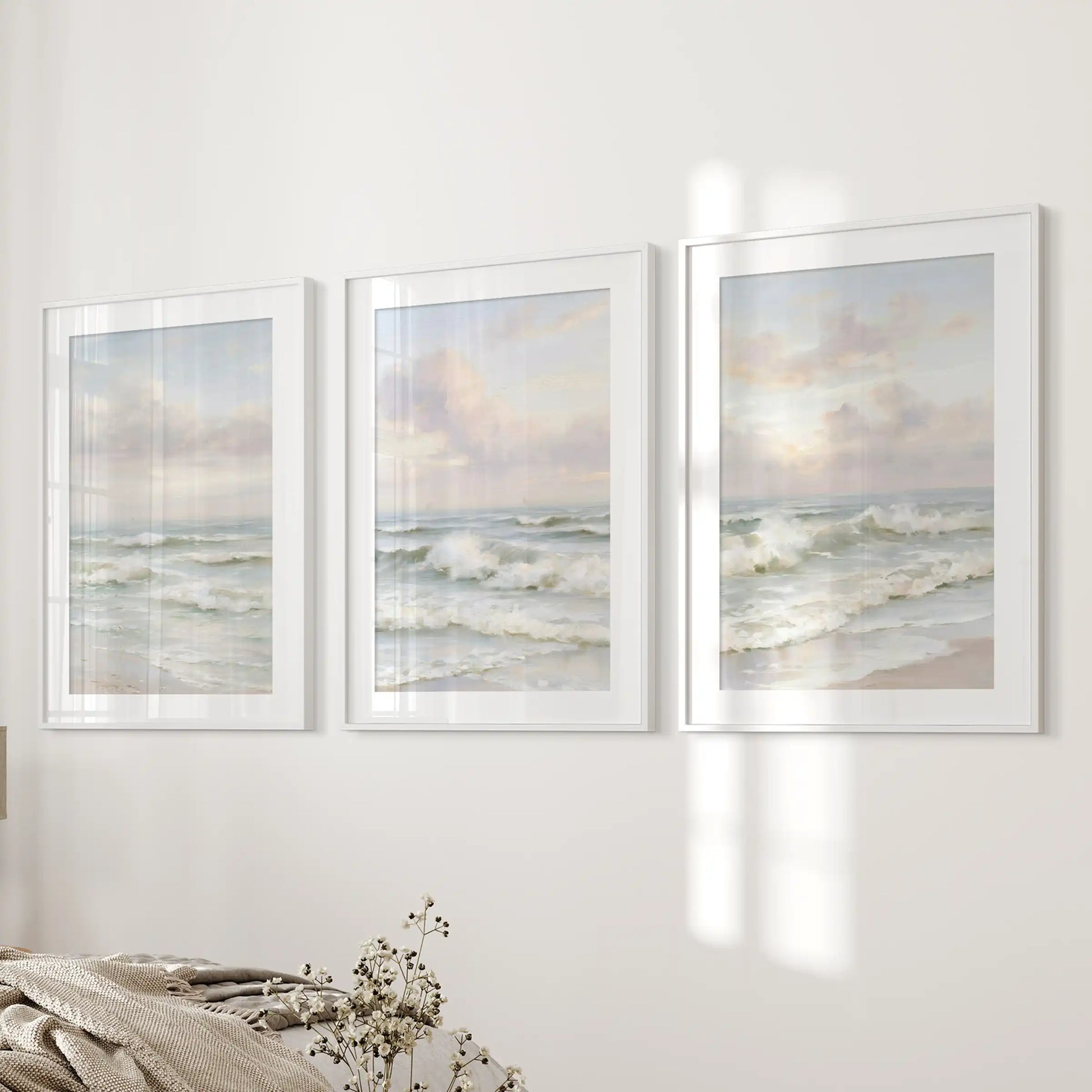 Three pastel-toned seascape prints in matted white frames bring gentle coastal light to the bedroom wall near the bed.