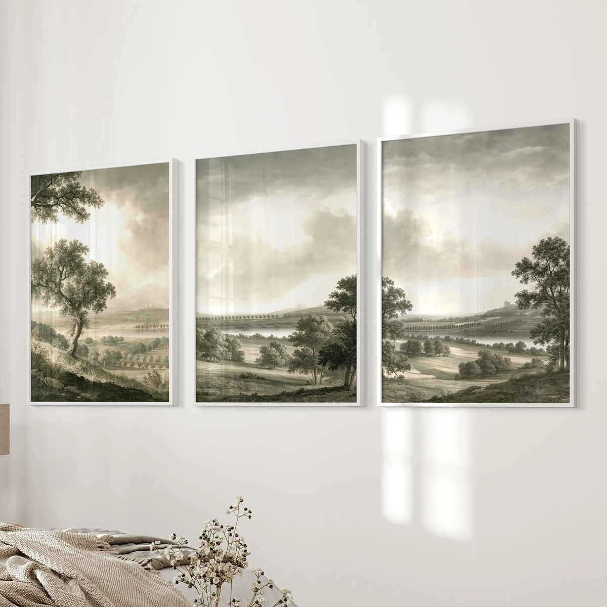 Three-piece pastoral countryside wall art set in white frames, displayed on a bedroom wall.