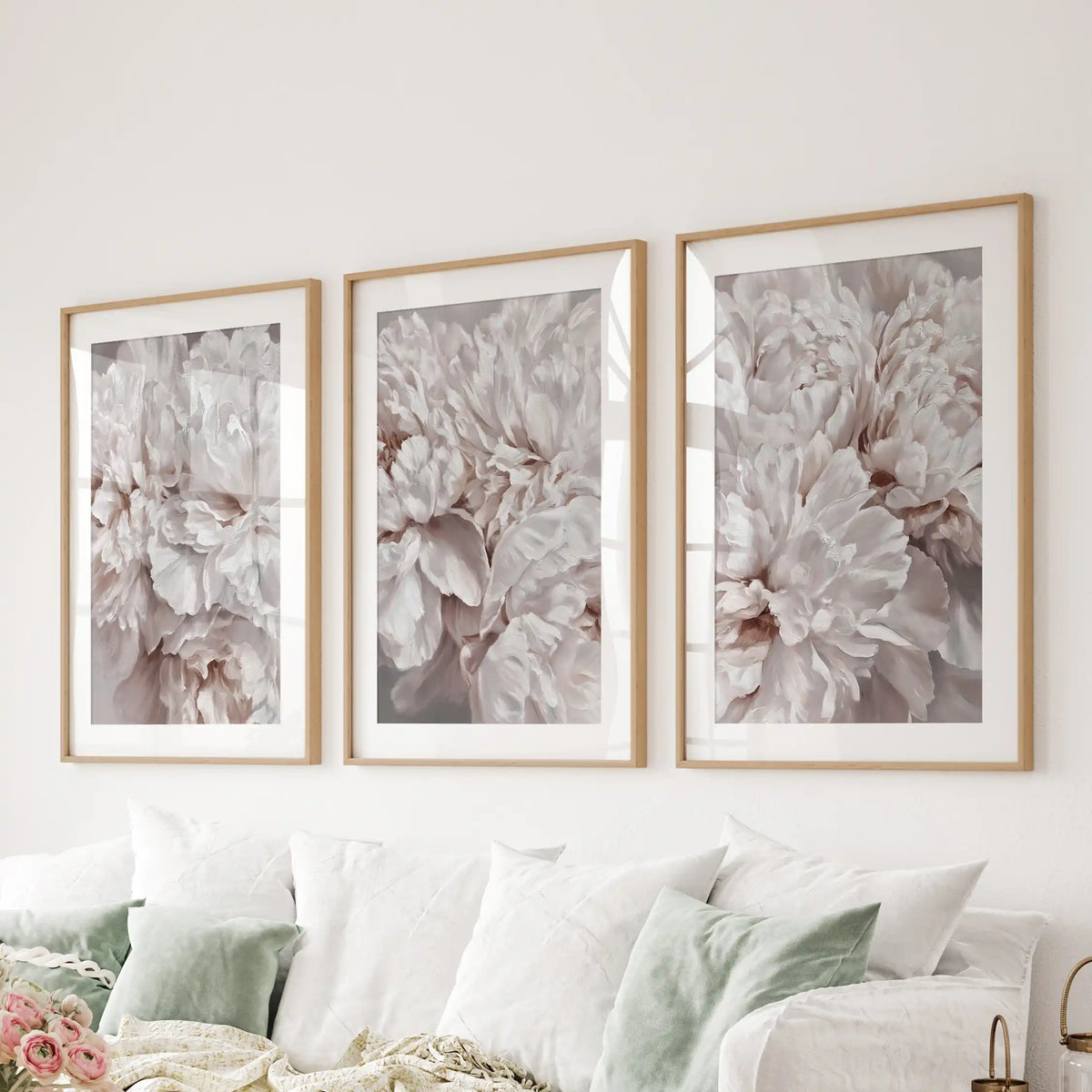 A set of three ruffled peony petal prints above a sofa, in oak frames with white mats.