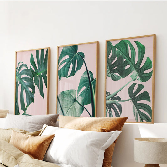 Three oak-framed pink monstera leaf prints create a relaxed gallery above the bed, lending the bedroom a soft boho botanical look.