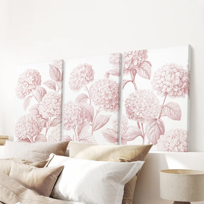 A set of three blush hydrangea canvases above a bed.