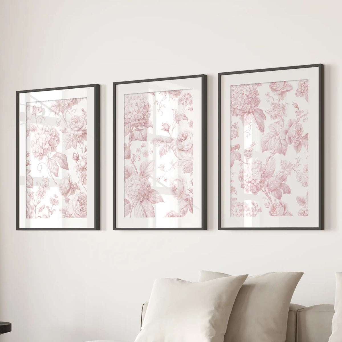 Blush roses, rounded hydrangea clusters and curling leaves fill three prints in black frames with white mats above a sofa.