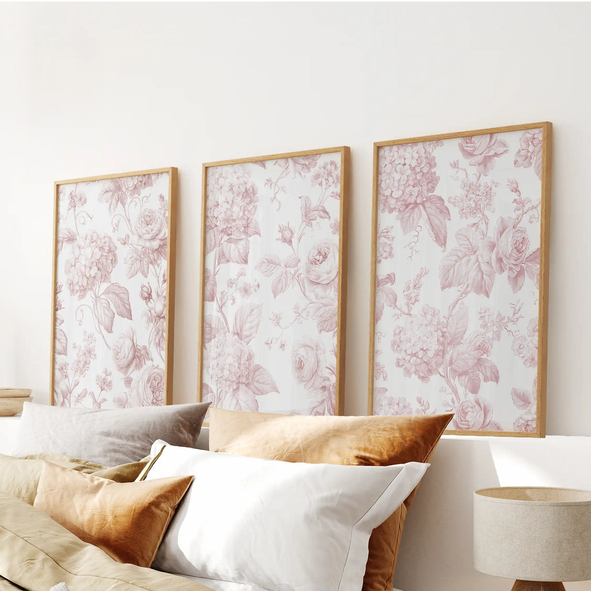 Blush floral pattern prints in oak frames, a set of three above a bed.