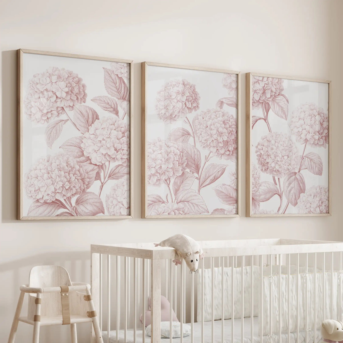 Above a white crib, three oak-framed prints show rounded hydrangea clusters branching through pale pink leaves.
