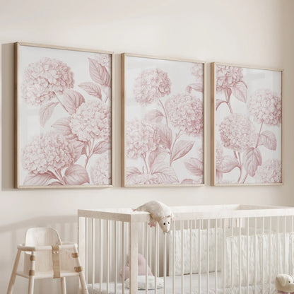 Above a white crib, three oak-framed prints show rounded hydrangea clusters branching through pale pink leaves.