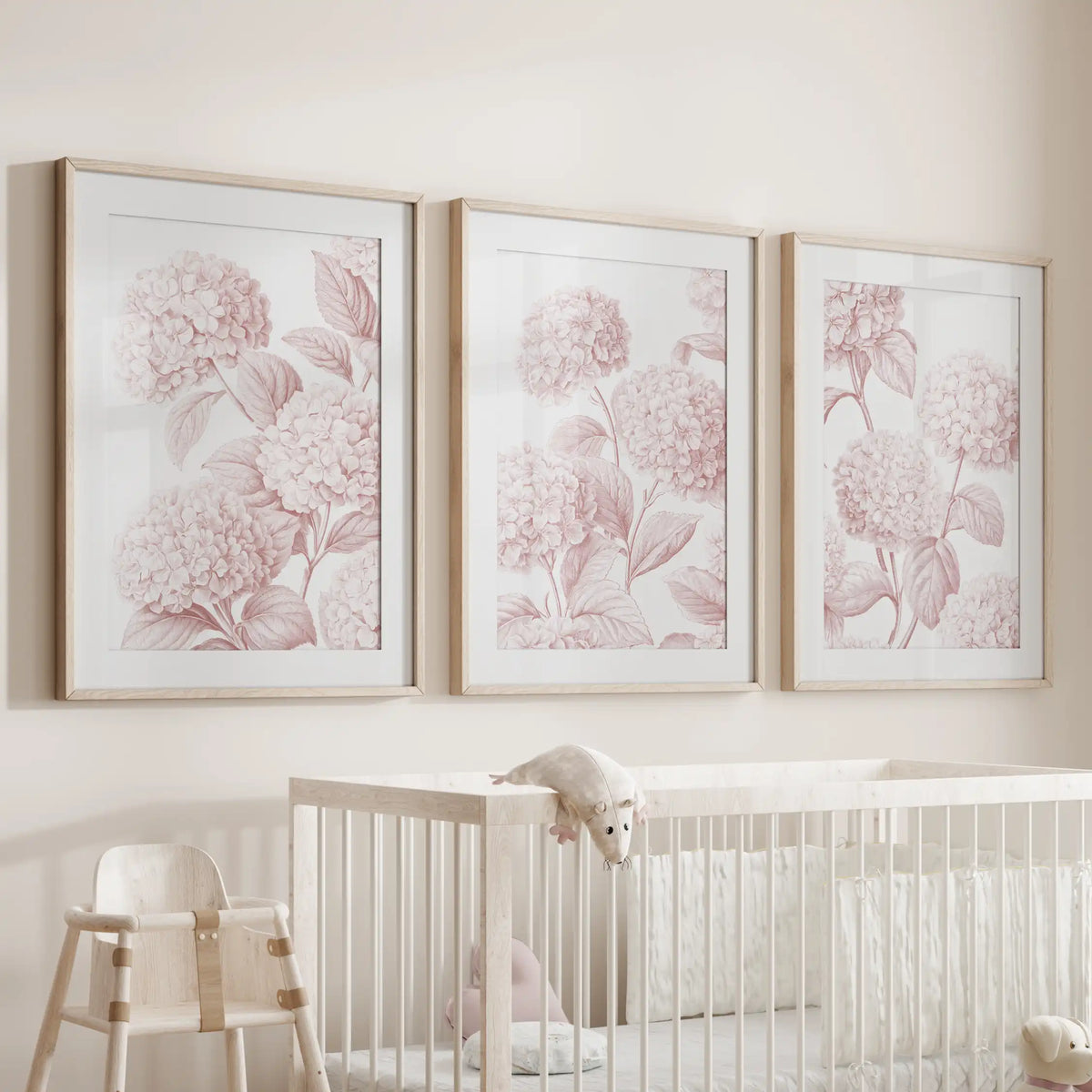 Oak frames and white mats surround three pink hydrangea prints above a crib, each showing rounded flowers and branching leaves.
