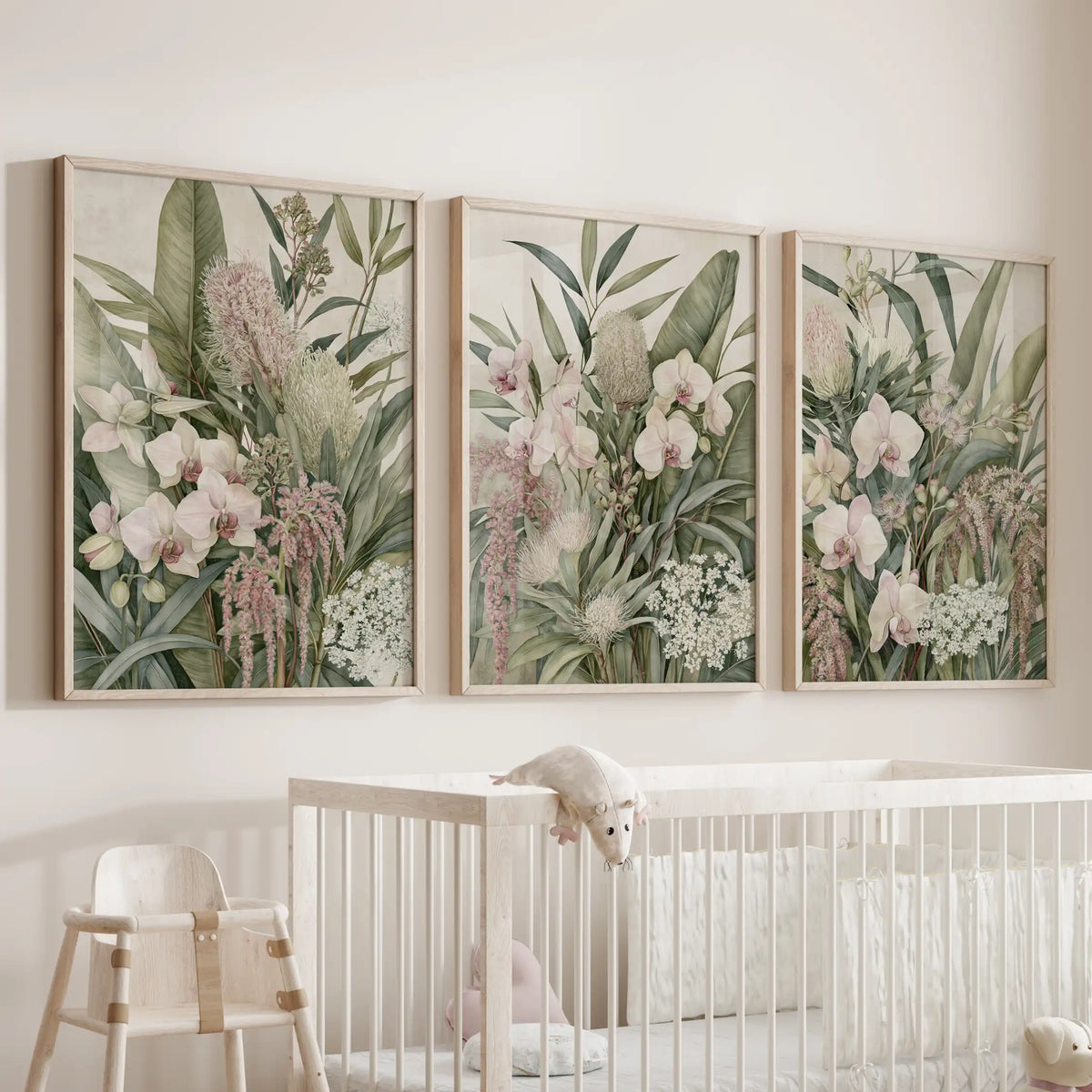 Dense green foliage and trailing pink flowers surround pale orchids in three oak-framed prints above a white crib.