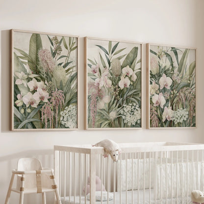 Dense green foliage and trailing pink flowers surround pale orchids in three oak-framed prints above a white crib.