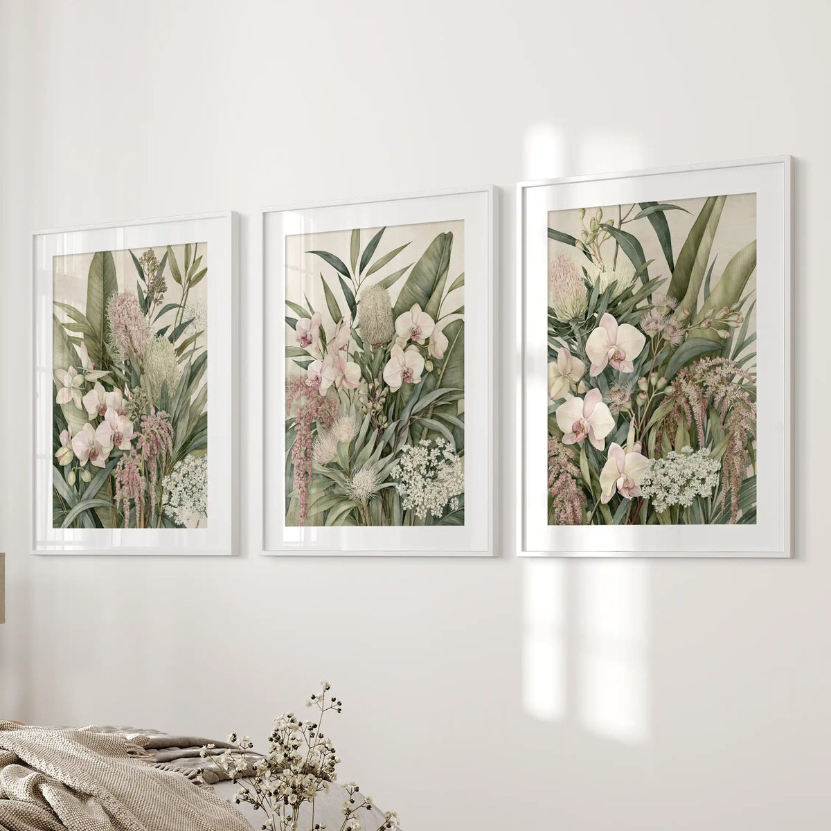 Three layered green leaf and orchid prints hang beside a bed, framed in white with white mats.