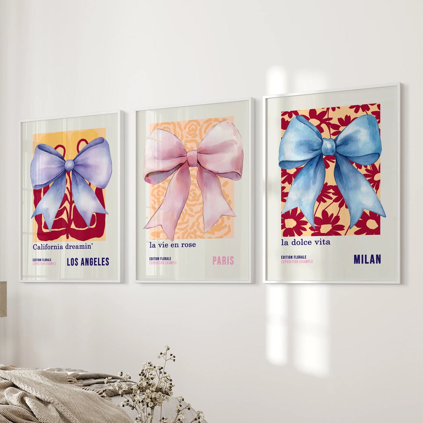 A gallery wall set of 3 ribbon-bow prints in white frames stacks neatly beside the bed, adding a touch of blue-pink charm to the bedroom.