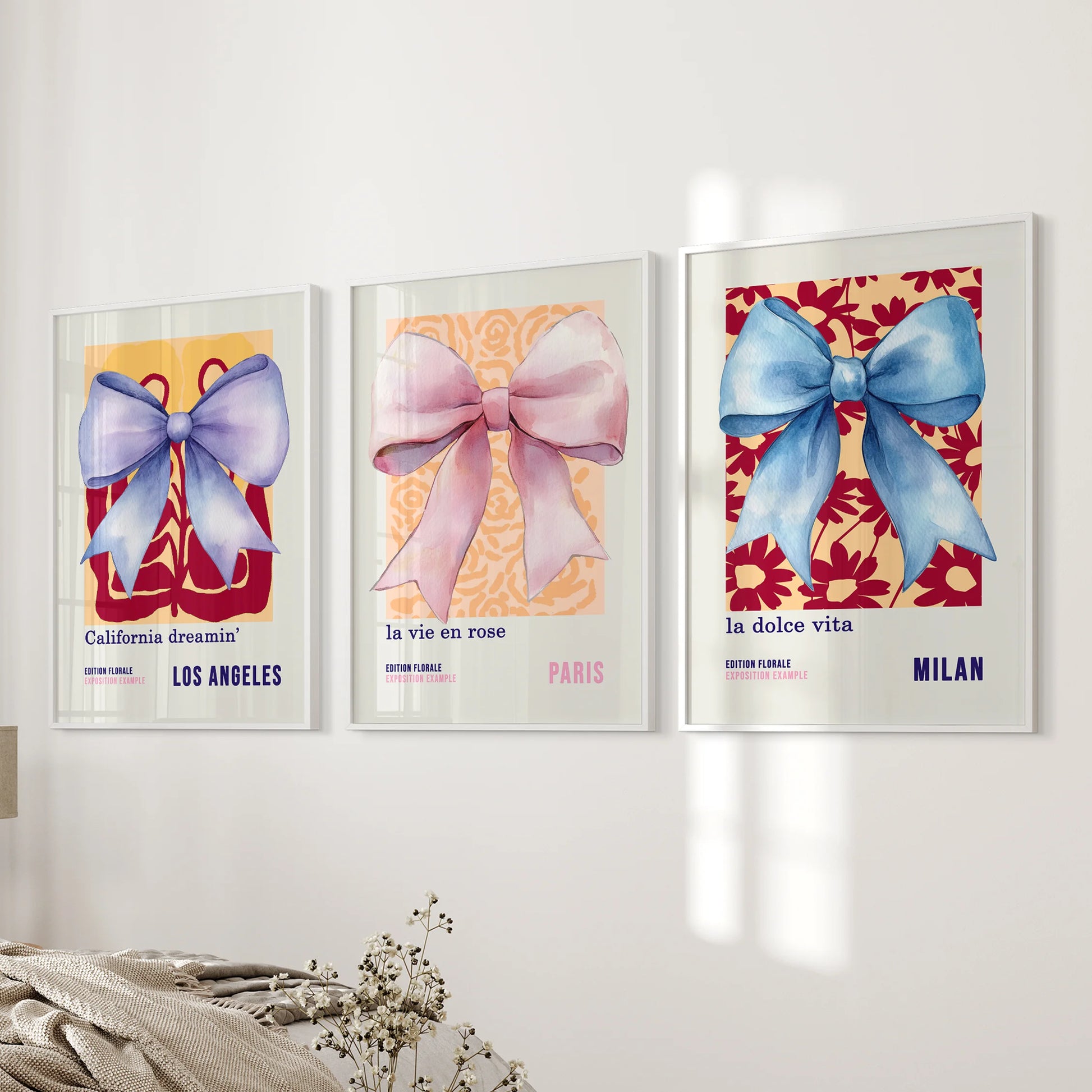 A gallery wall set of 3 ribbon-bow prints in white frames stacks neatly beside the bed, adding a touch of blue-pink charm to the bedroom.