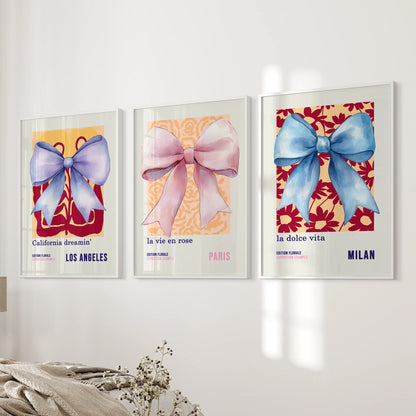 A gallery wall set of 3 ribbon-bow prints in white frames stacks neatly beside the bed, adding a touch of blue-pink charm to the bedroom.