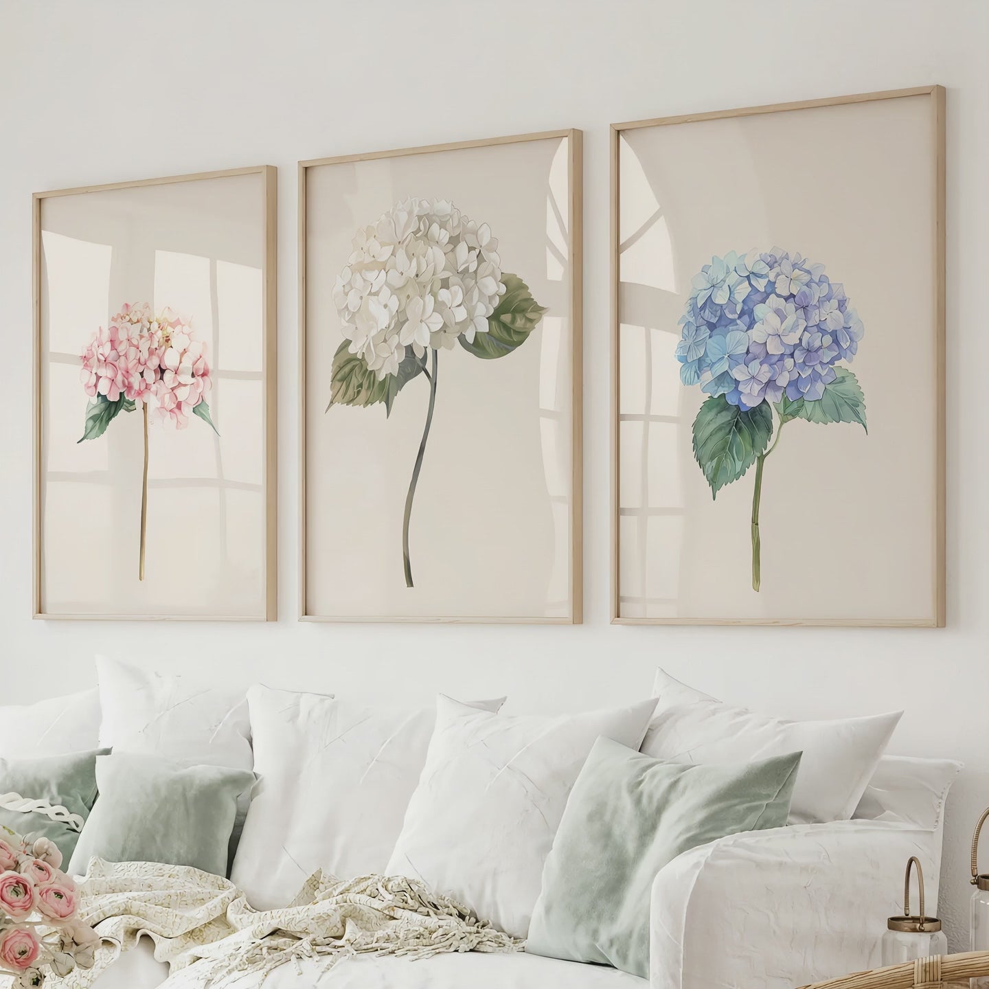 Three pink, white and blue hydrangea prints in natural wood frames above a white sofa