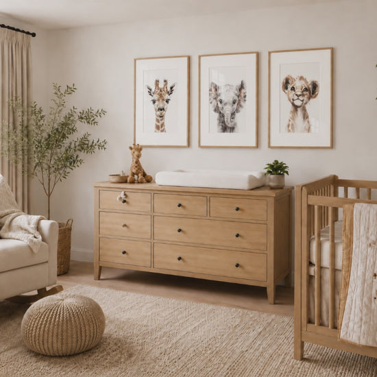 Slow camera push-in toward three baby animal prints — a giraffe, elephant and lion — in natural wood frames above a nursery dresser.