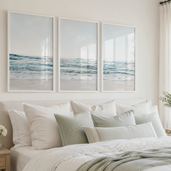 Three blue ocean prints in white frames hang above a bright neutral bed as the camera slowly moves closer